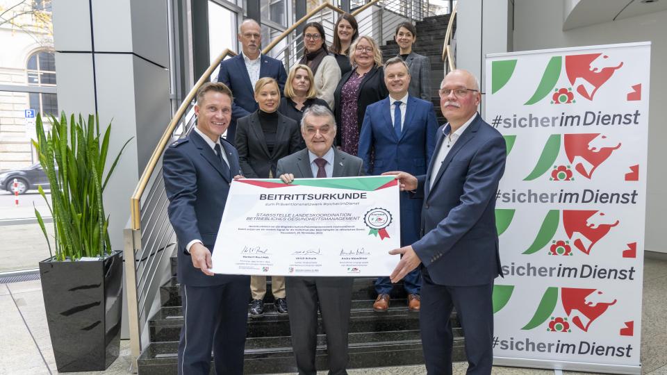 Gruppenfoto: Innenminister Herbert Reul sowie Vertreterinnen und Vertreter der Stabsstelle Landeskoordination BGM und #sicherimDienst mit der Beitrittsurkunde
