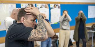 Ein Mann im schwarzen T-Shirt hält seine tätowierten Arme schützend vor seine Stirn